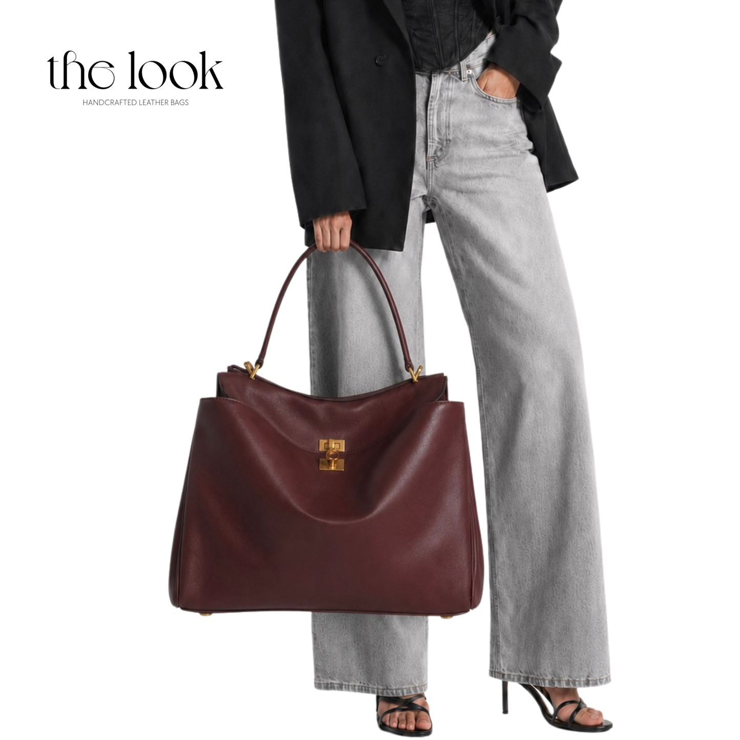 A woman wearing light-wash wide-leg jeans, a black blazer, and black sandals carries a large burgundy leather handbag with gold hardware.