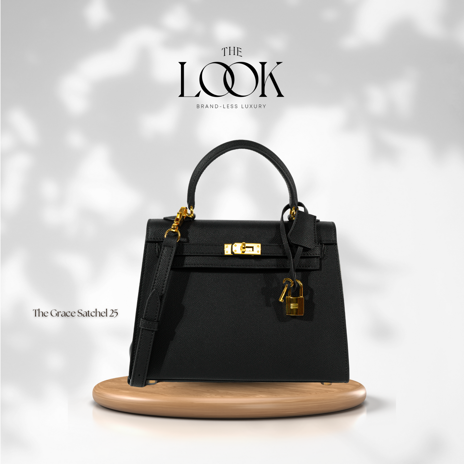 A black The Grace 25 satchel Epsom leather handbag with gold hardware, displayed on a wooden platform, against a white background with the logo 'The Look' at the top. | The Look Officiel