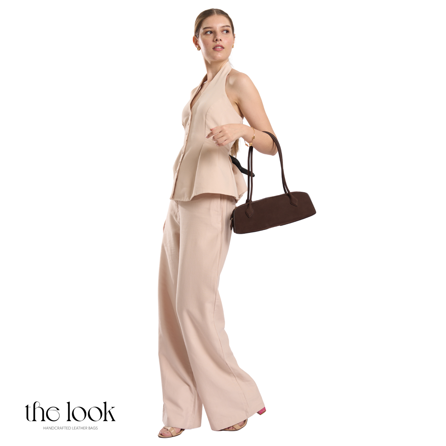 Woman in beige outfit holding a brown handbag on a white background | The Look Officiel