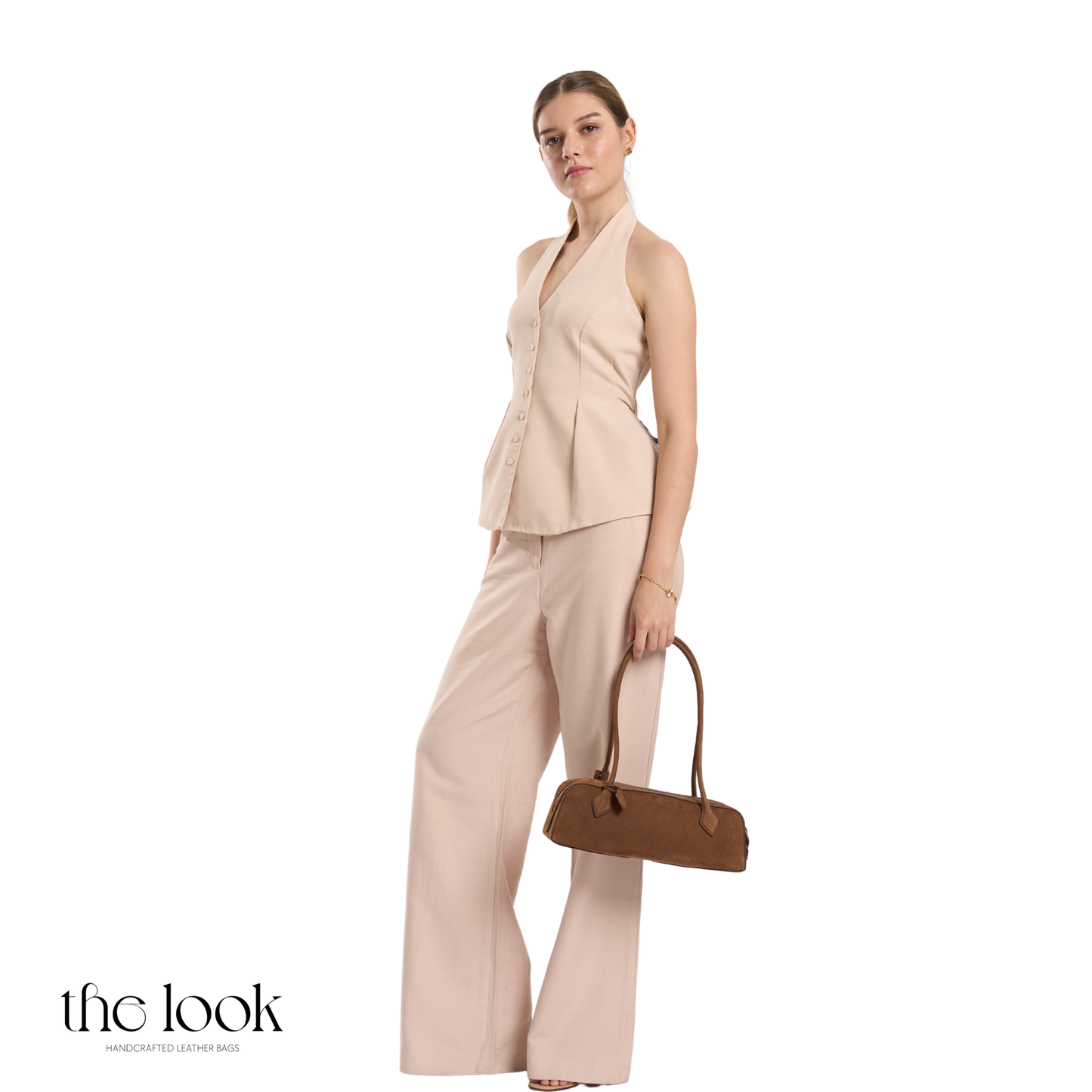 Woman in a beige outfit holding a brown handbag on a white background | The Look Officiel