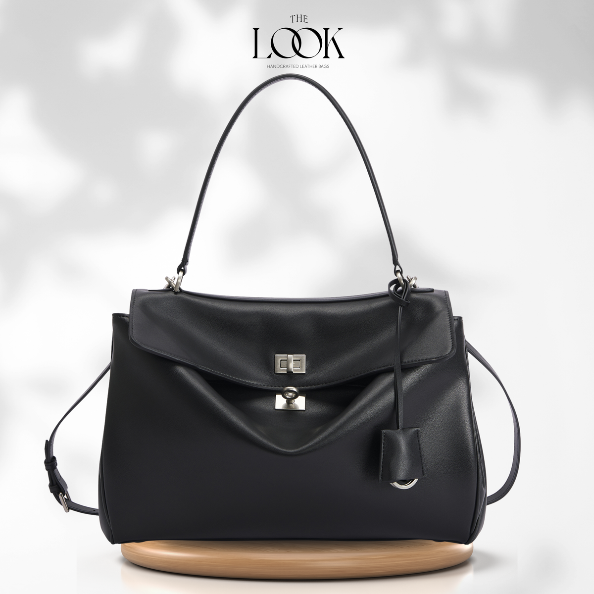 A black leather handbag with a structured flap front, silver-tone hardware, a top handle, and a detachable shoulder strap.