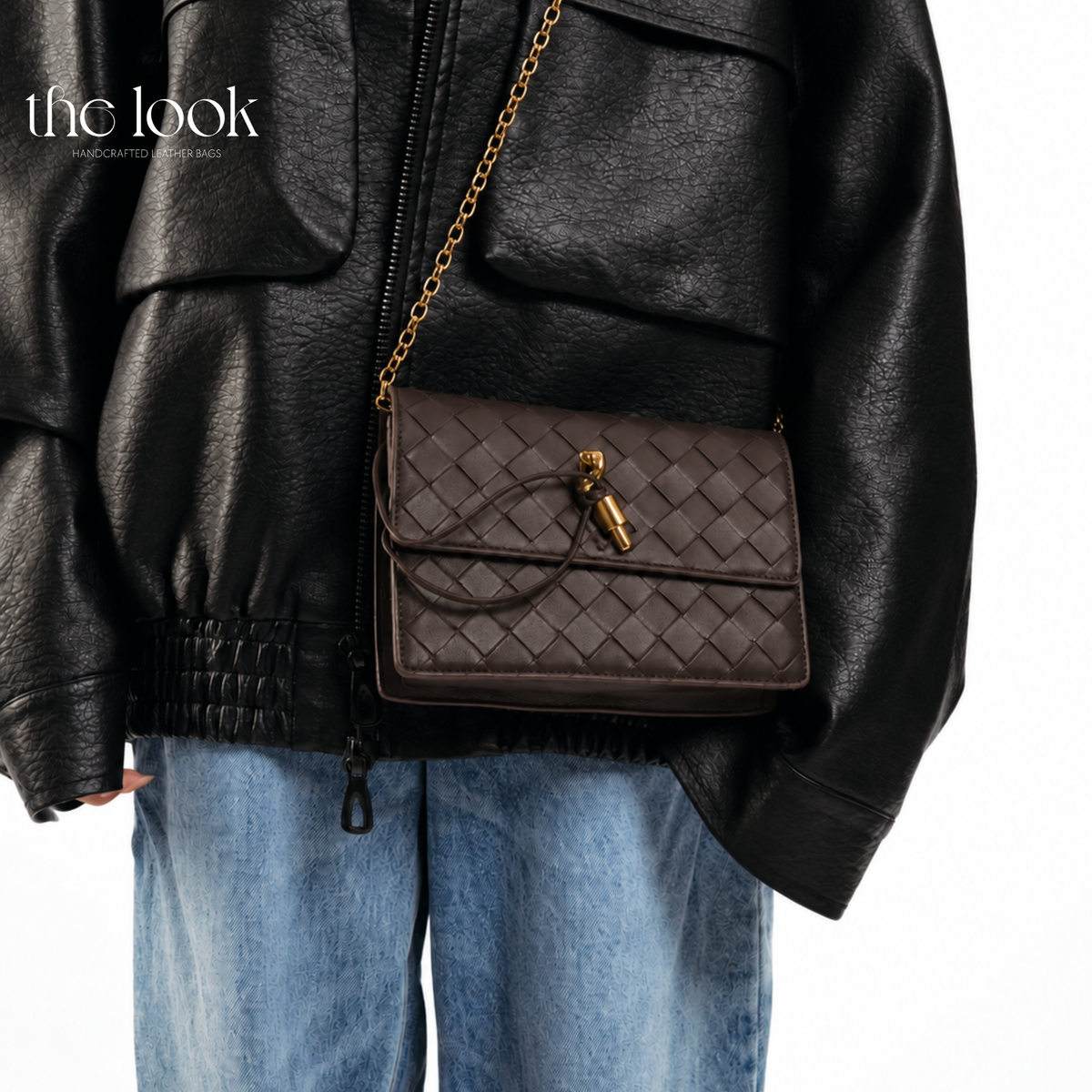 The Loop Wallet on Chain in Ebene, worn crossbody with a black leather jacket and blue jeans, showing its woven leather and gold-tone chain.