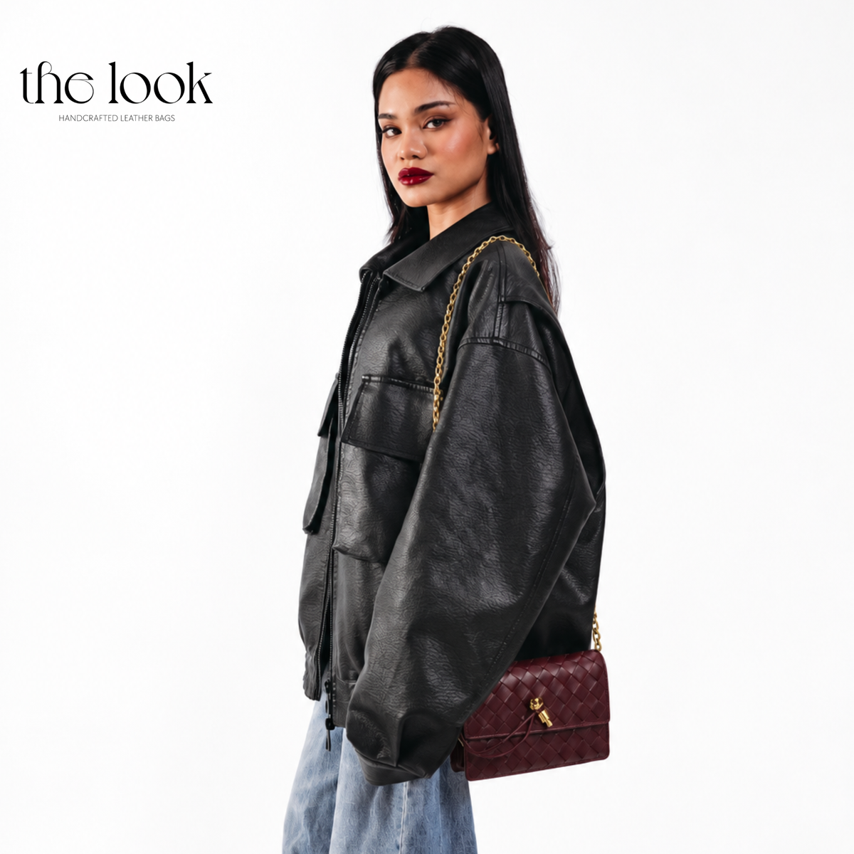 The Loop Wallet on Chain in Burgundy, worn crossbody with a black leather jacket and blue jeans, showing its woven leather and gold-tone hardware.