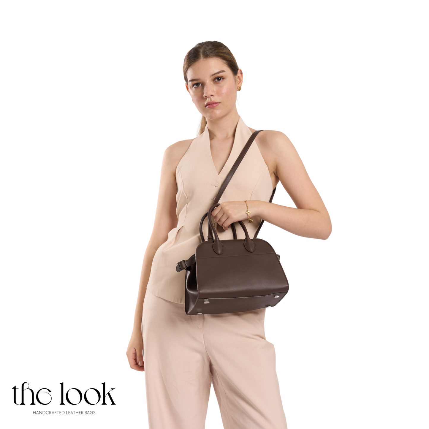 Woman holding a brown leather handbag against a white background | The Look Officiel