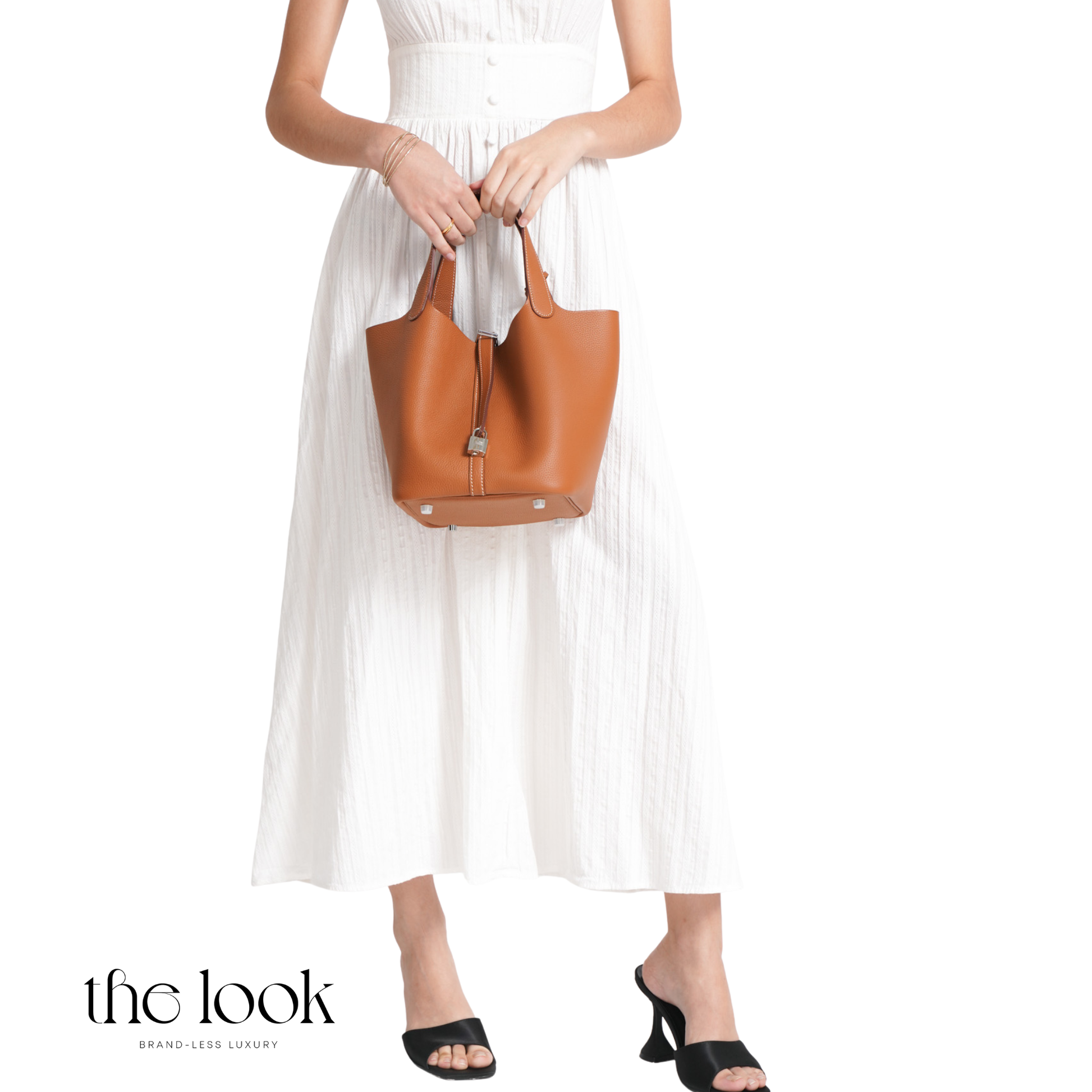 Woman holding a brown leather handbag wearing a white dress on a white background with 'the look' branding. | The Look Officiel