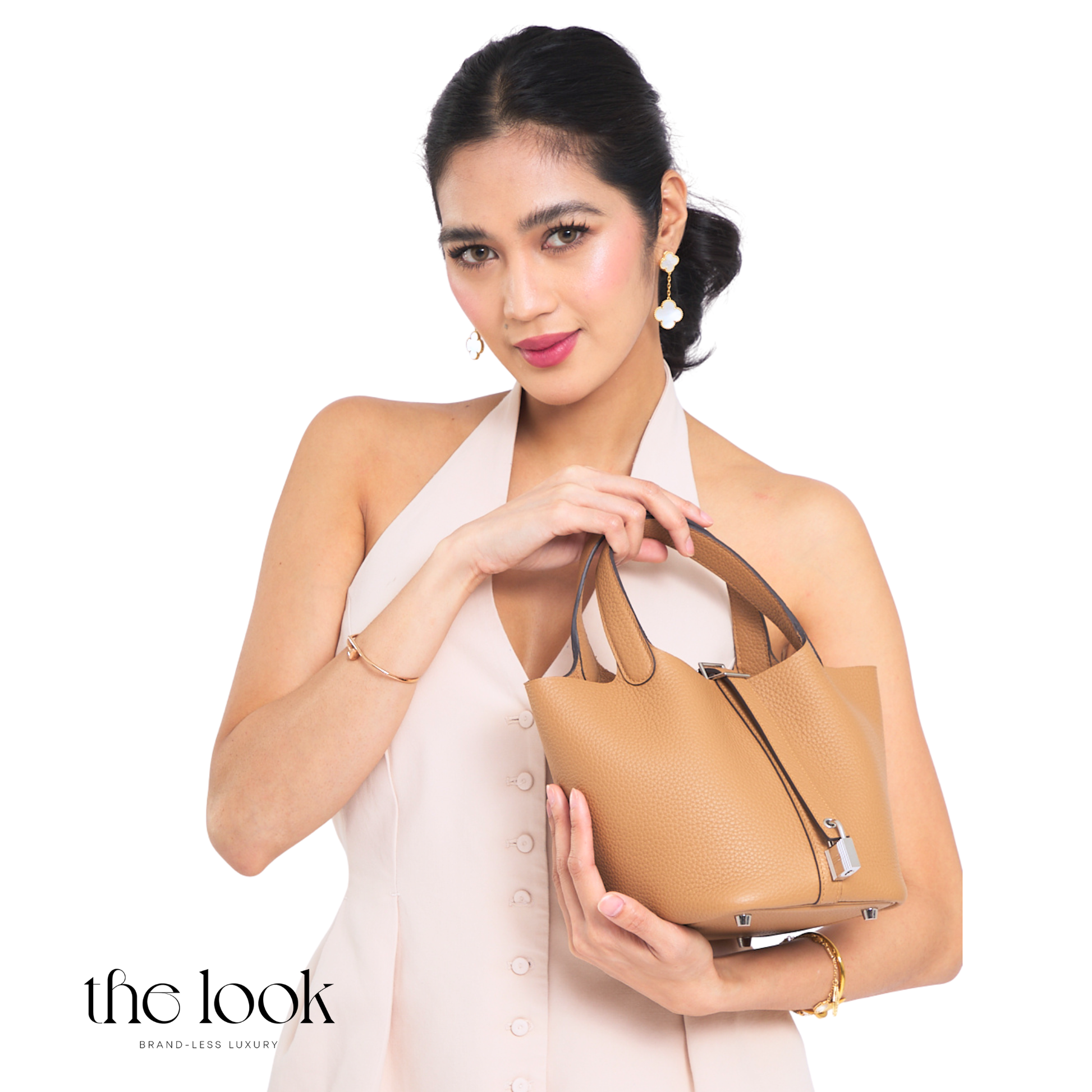 Woman holding a tan handbag against a white background with 'the look' branding. | The Look Officiel
