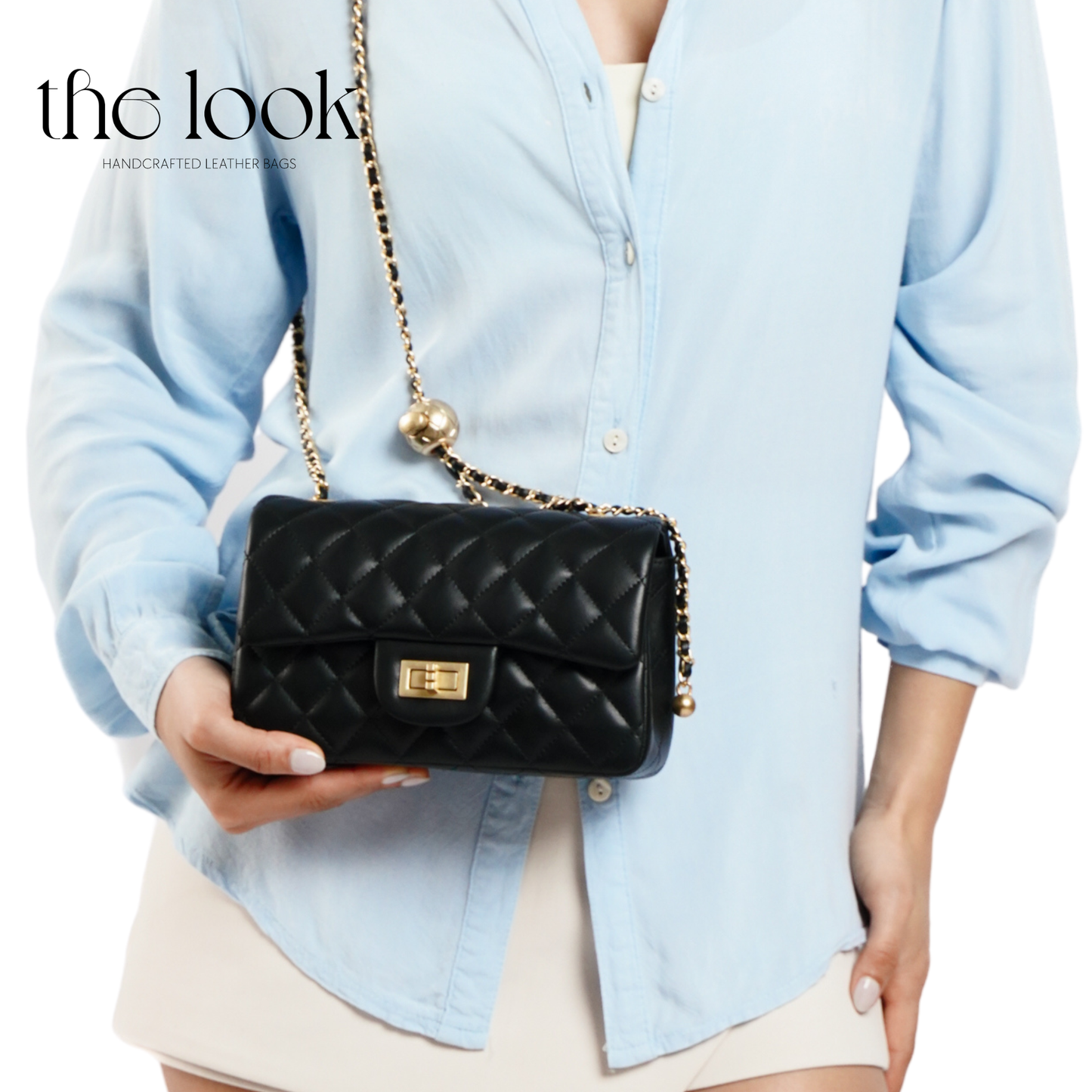 Person holding a black quilted handbag with a gold chain strap, wearing a light blue shirt. | The Look Officiel