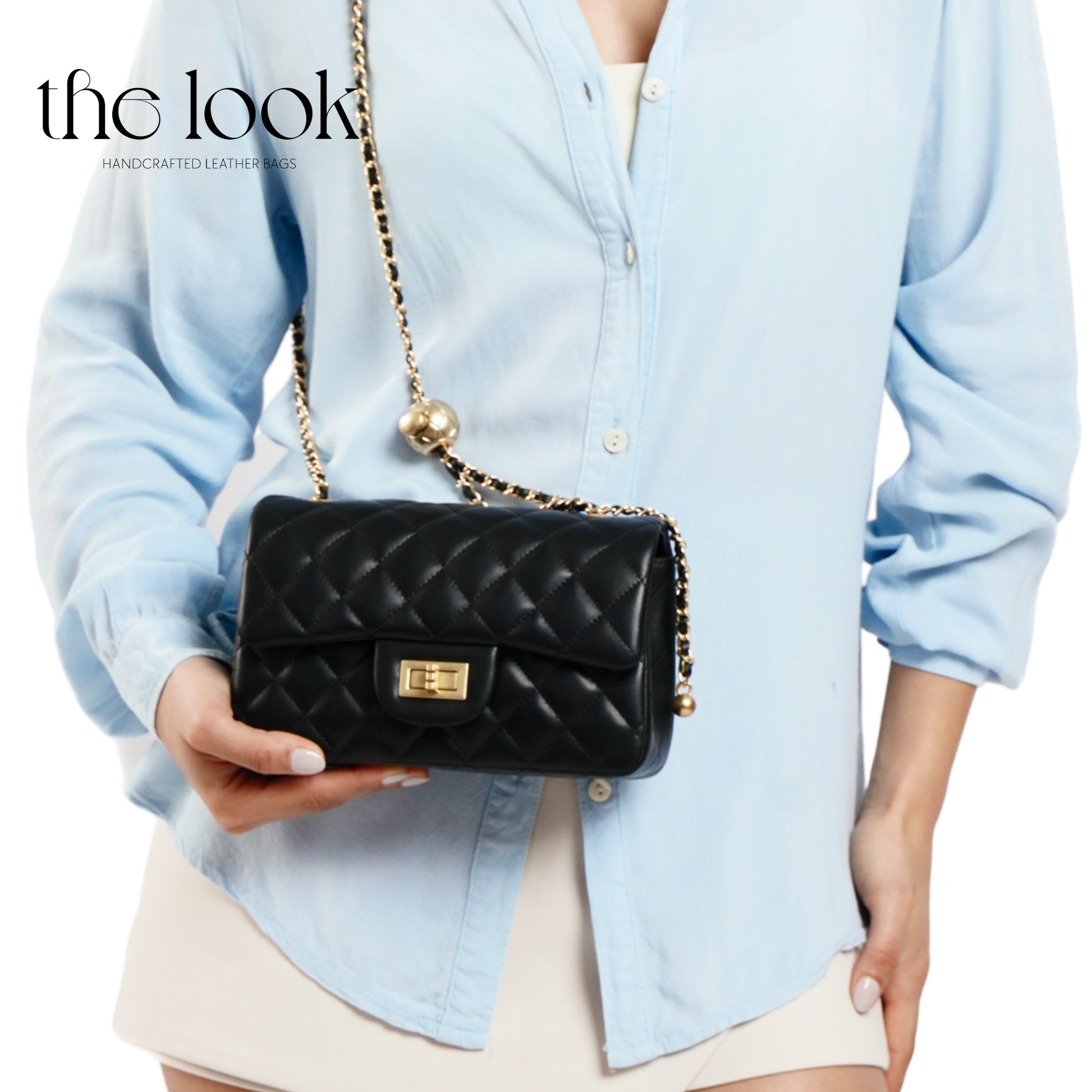 Person holding a black quilted handbag with a gold chain strap, wearing a light blue shirt. | The Look Officiel