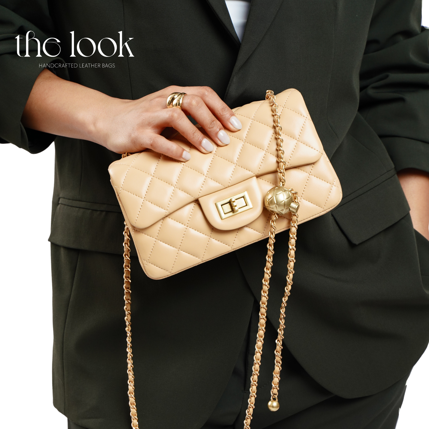 Beige quilted handbag with gold chain held by a person in a black suit. | The Look Officiel