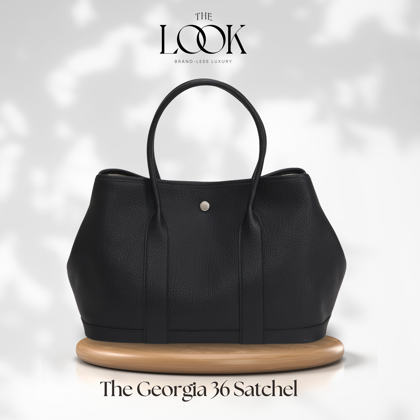Black satchel bag on a wooden stand with 'The Look' brand logo above it. | The Look Officiel