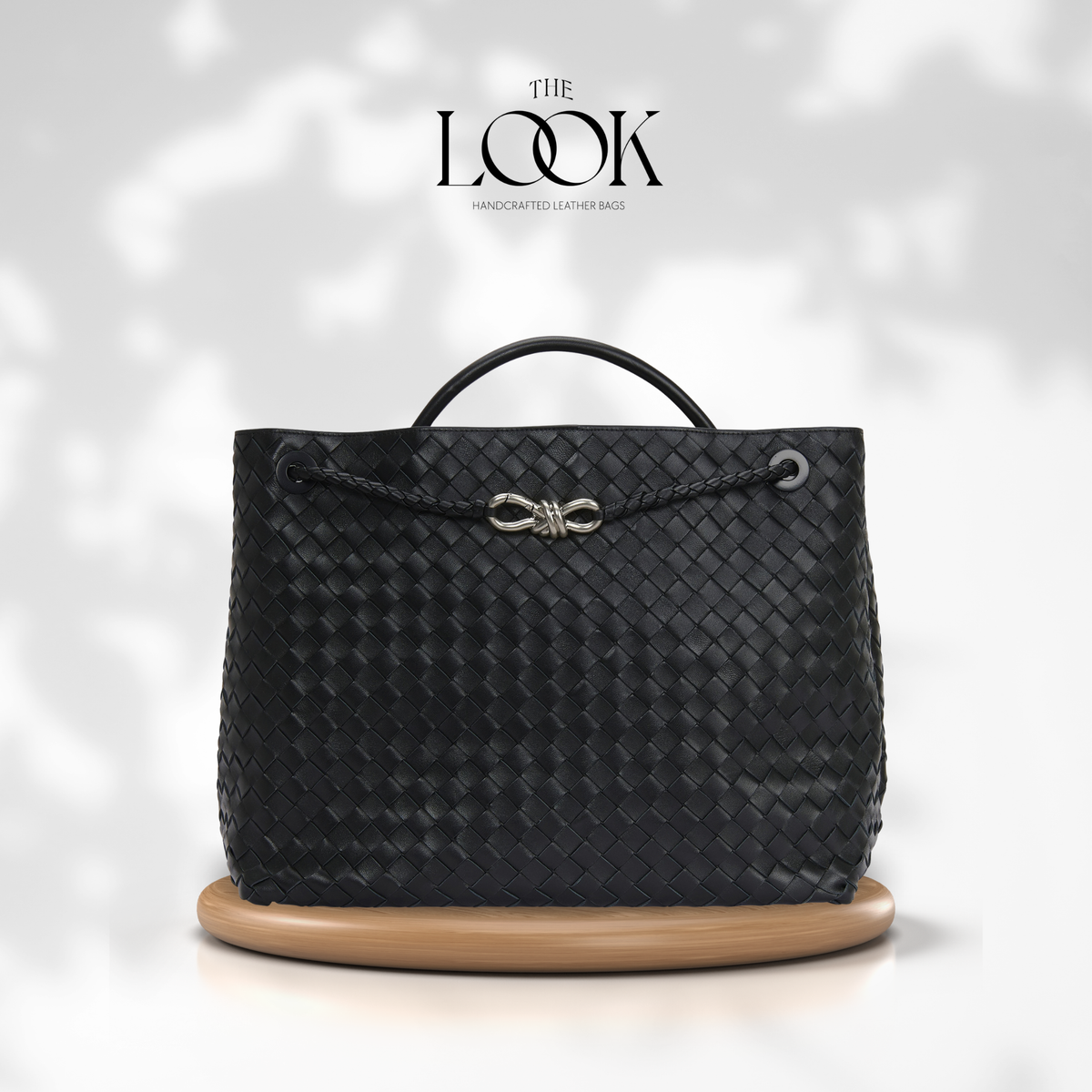 The Loop Jumbo Satchel in black woven leather with silver hardware and top handle, front view.