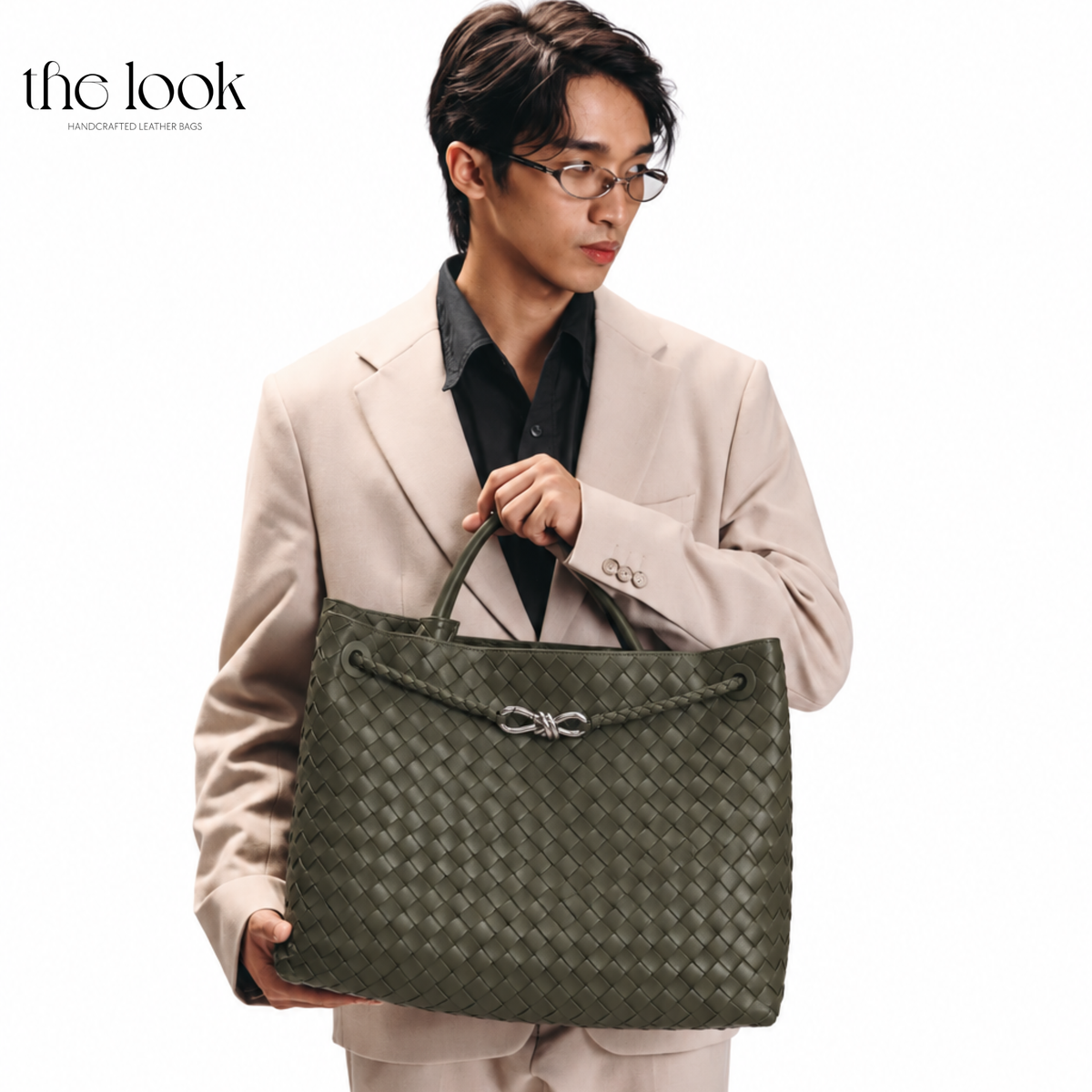 Model carrying The Loop Jumbo Satchel in olive woven leather with silver hardware by the top handles.
