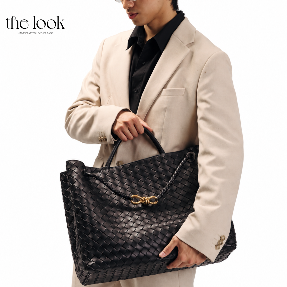 Model carrying The Loop Jumbo Satchel in black woven leather with gold hardware by the top handles.