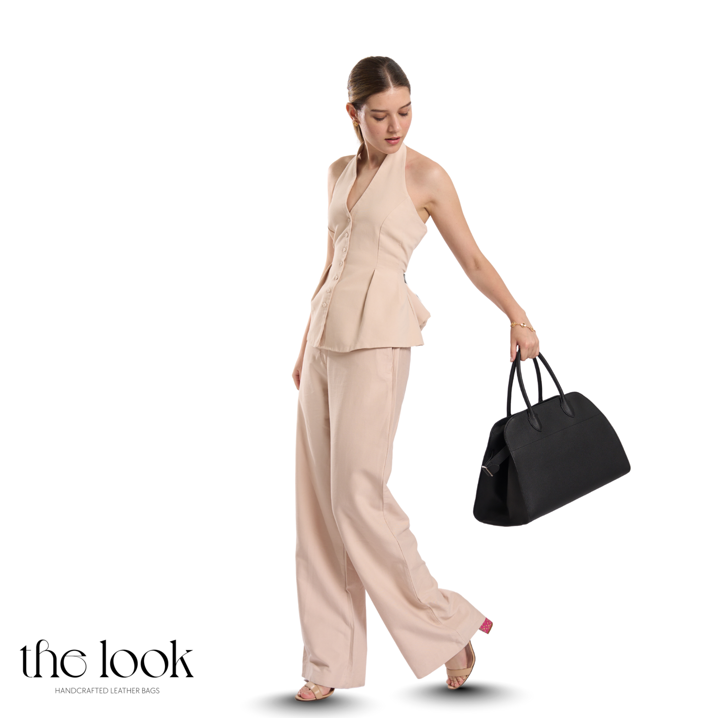 Woman in a beige outfit holding a black handbag on a white background | The Look Officiel