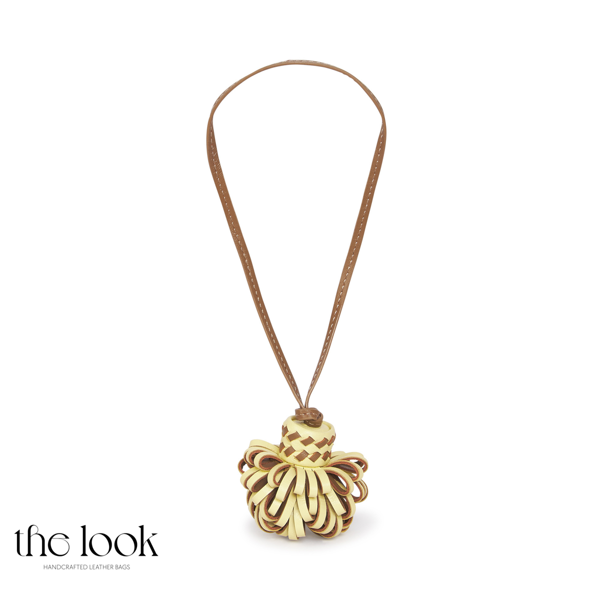 Pompette Pastel Yellow leather bag charm with brown accents, a woven-look band, and a tan hanging loop | The Look Officiel