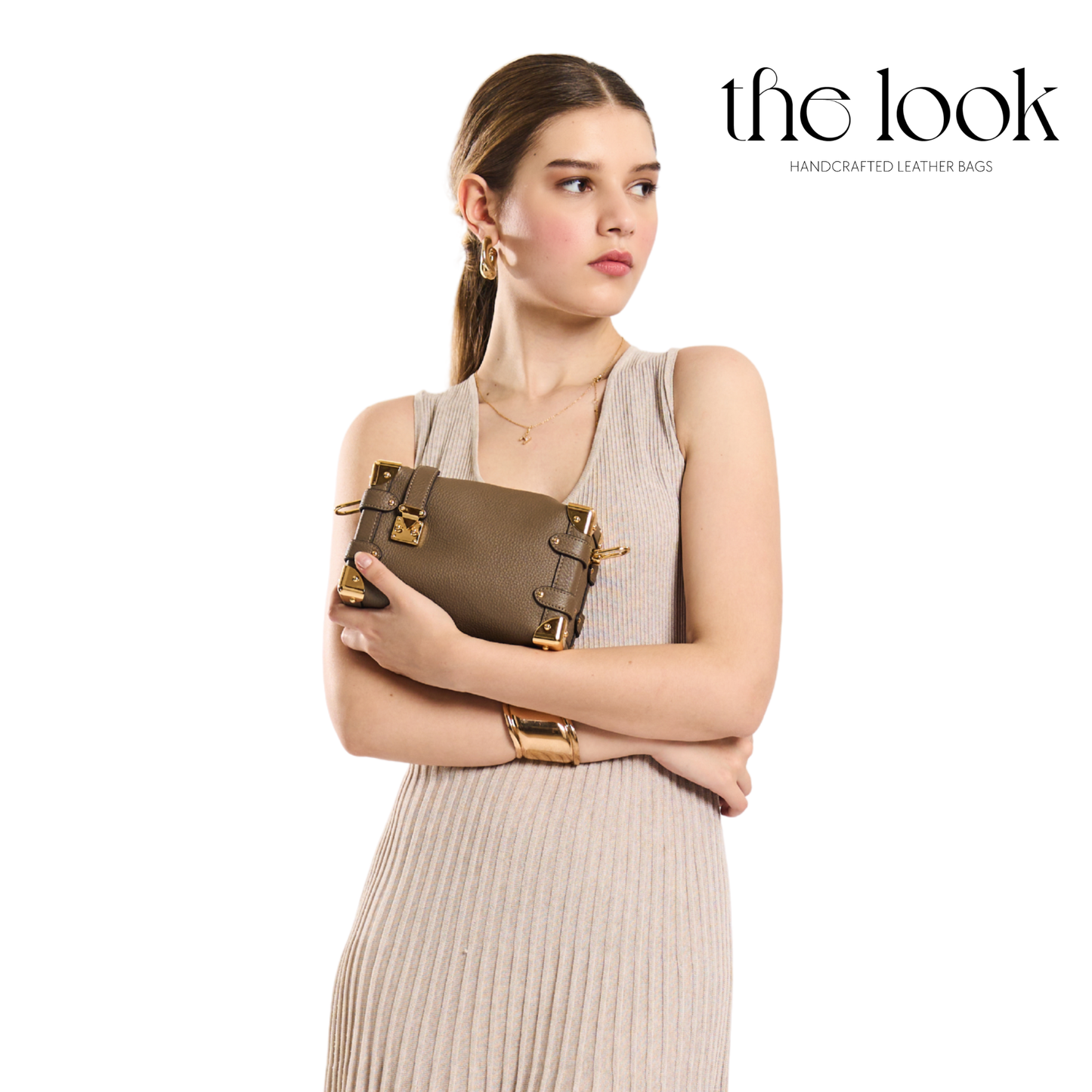 Woman holding a brown leather handbag with 'the look' branding on a white background. | The Look Officiel