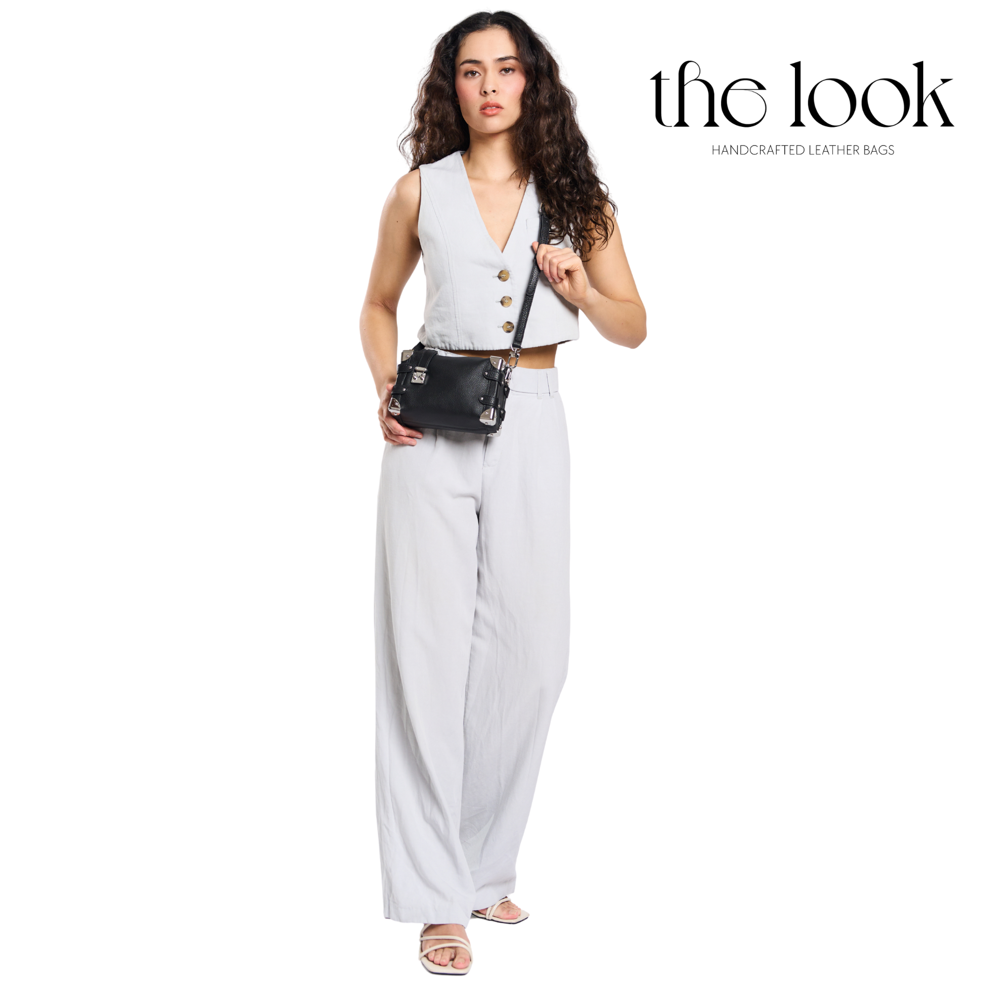 Woman holding a black handbag with 'the look' brand on a white background. | The Look Officiel