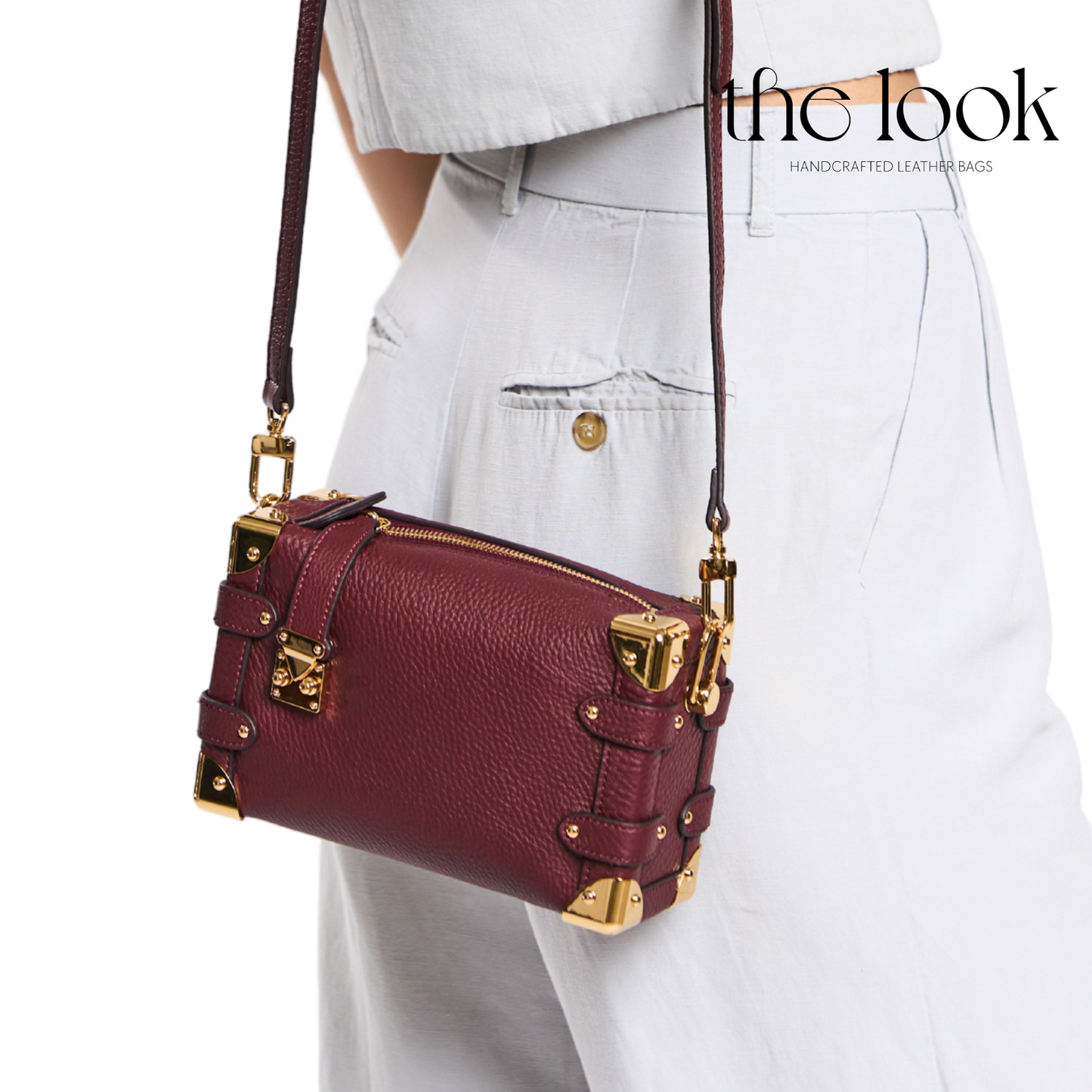 Maroon leather handbag with gold accents worn by a person on a white background, featuring 'the look' brand. | The Look Officiel
