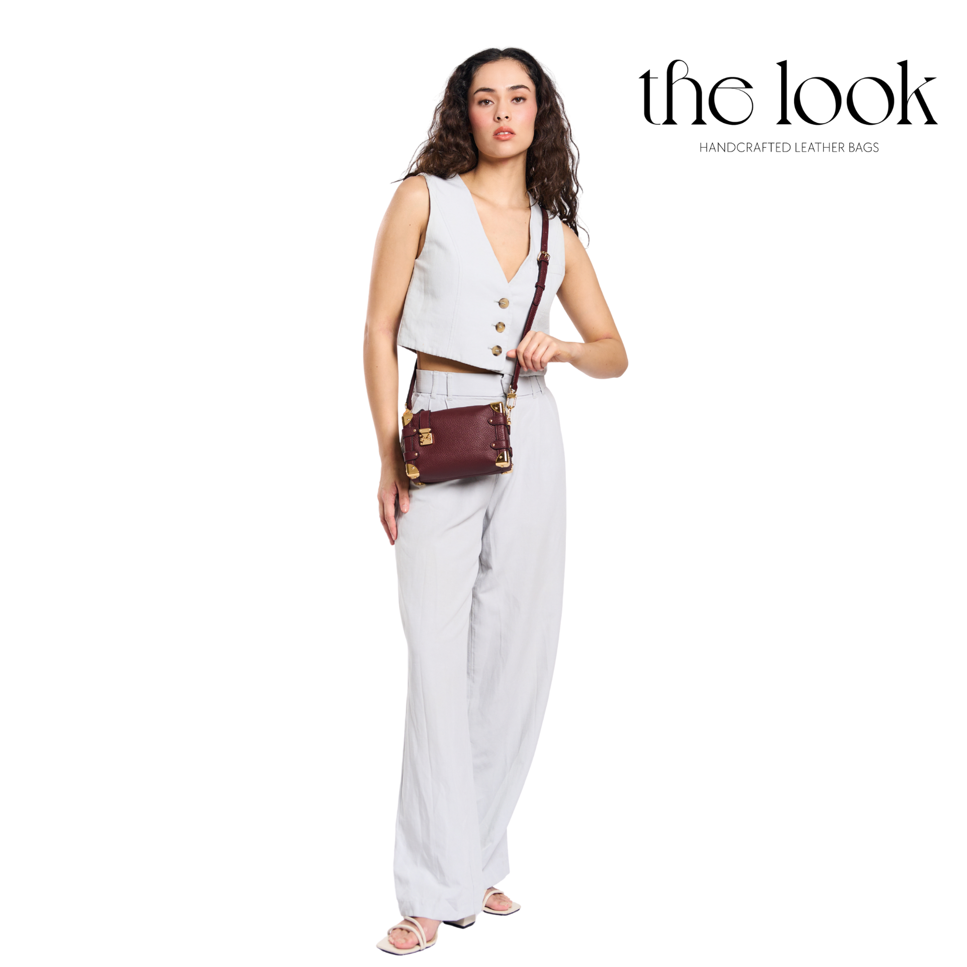 Woman holding a brown leather handbag with 'the look' branding on a white background. | The Look Officiel