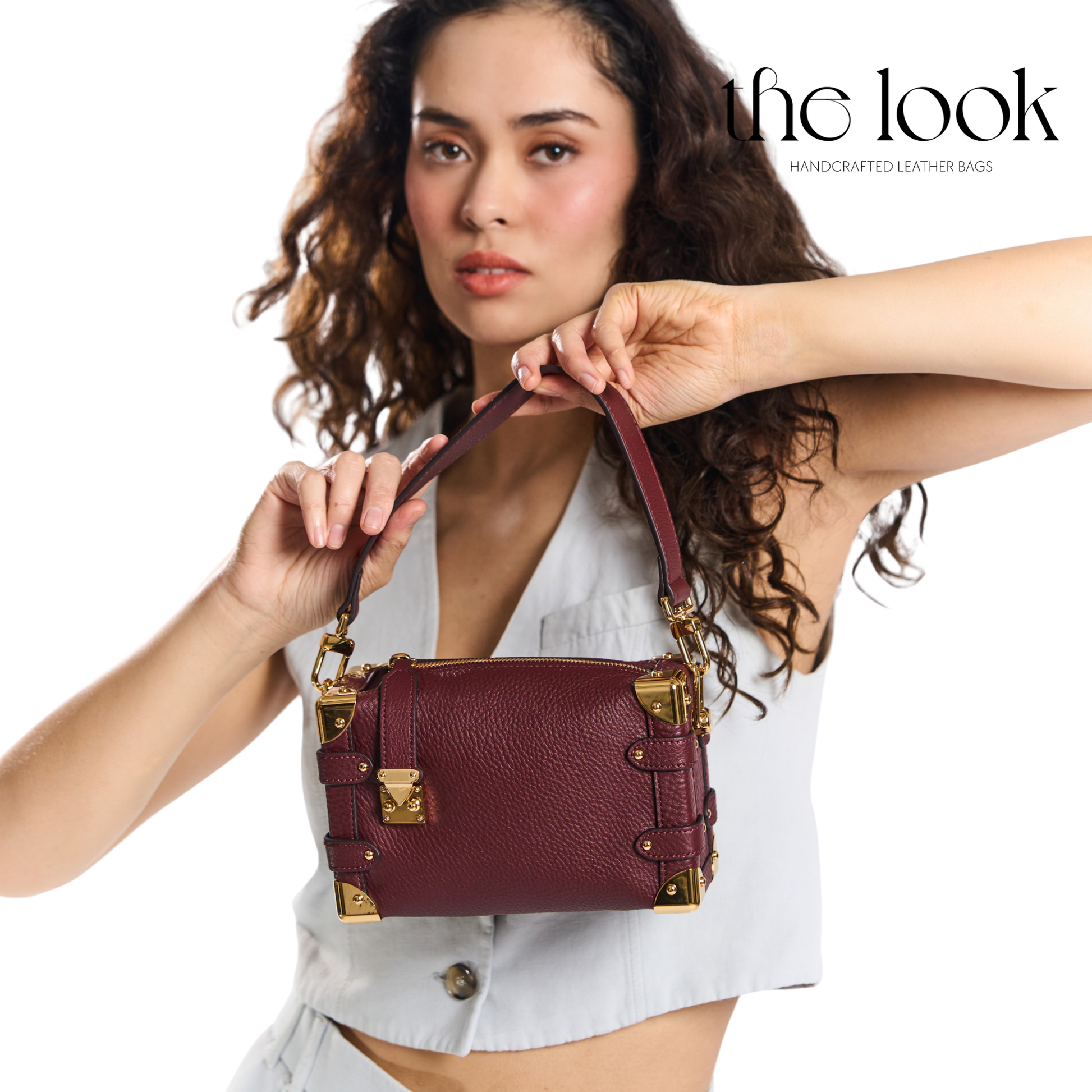 Woman holding a maroon leather handbag with gold accents, branded 'the look'. | The Look Officiel