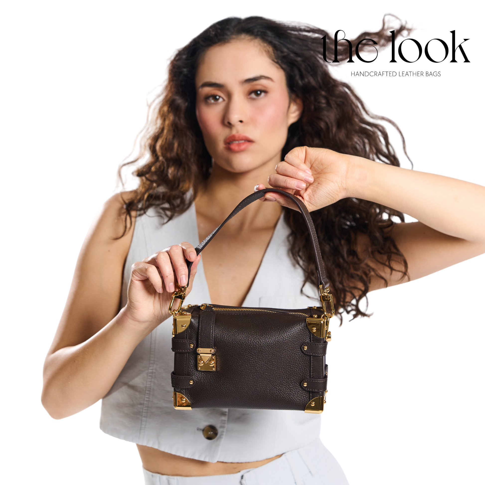 Woman holding a brown leather handbag with gold accents, branded 'the look'. | The Look Officiel