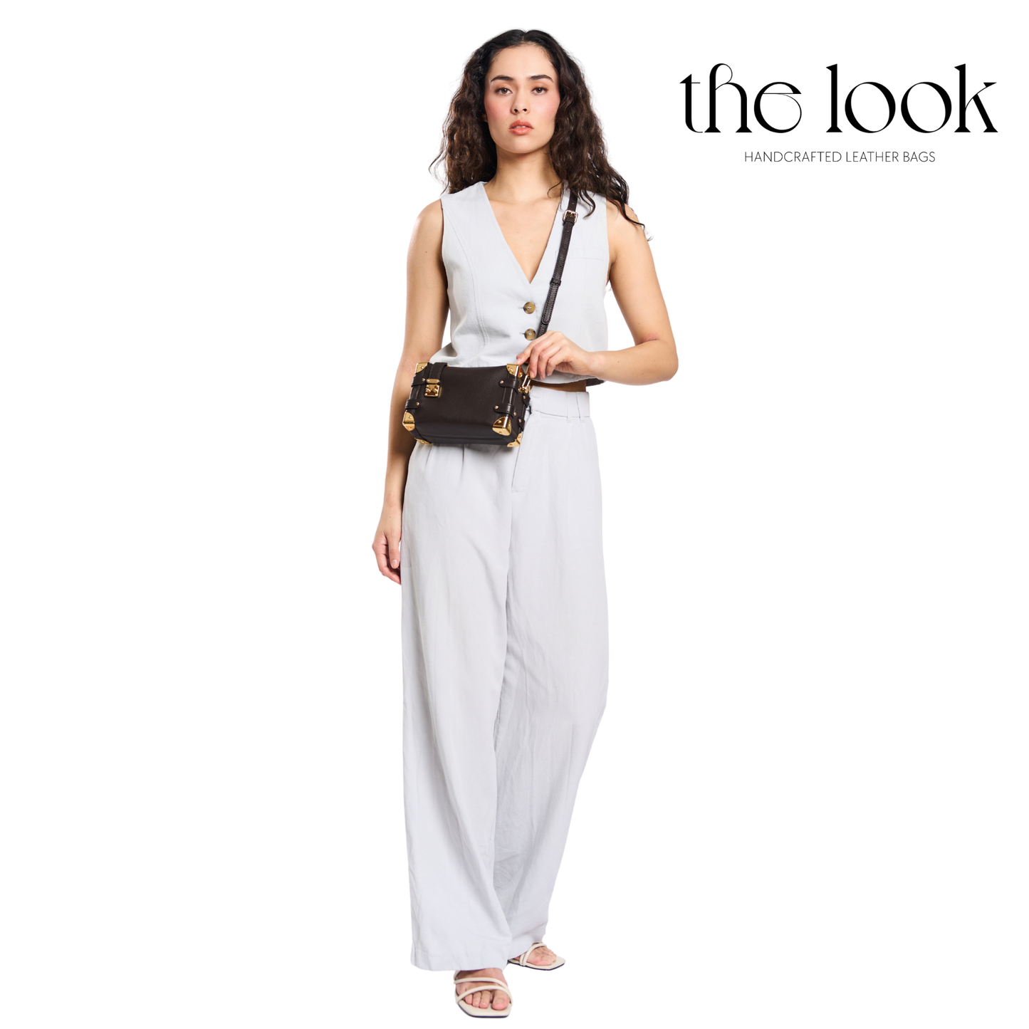 Woman in a white outfit holding a black leather bag with 'the look' branding. | The Look Officiel