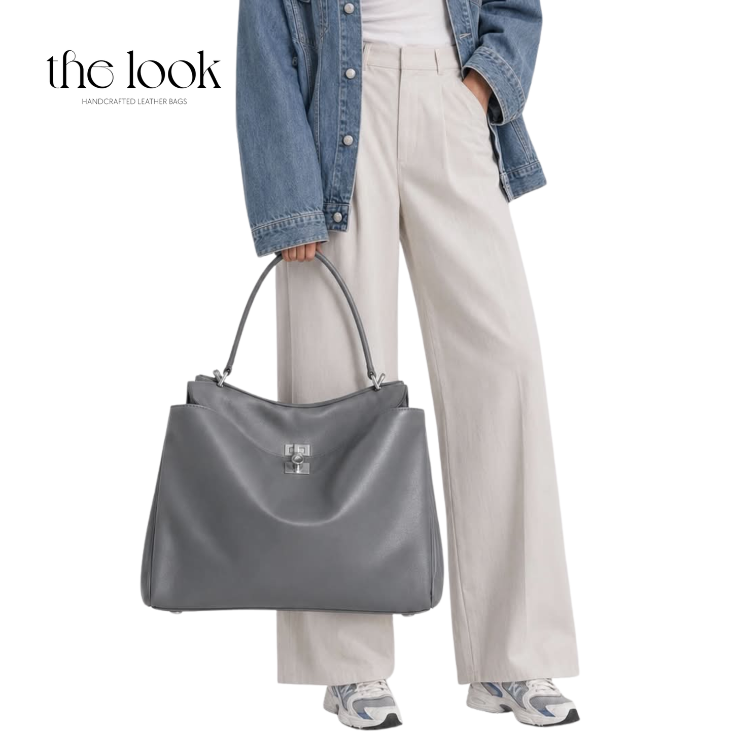 A gray leather tote bag with a silver-tone, held by a model wearing a denim jacket, cream wide-leg trousers, and sneakers.