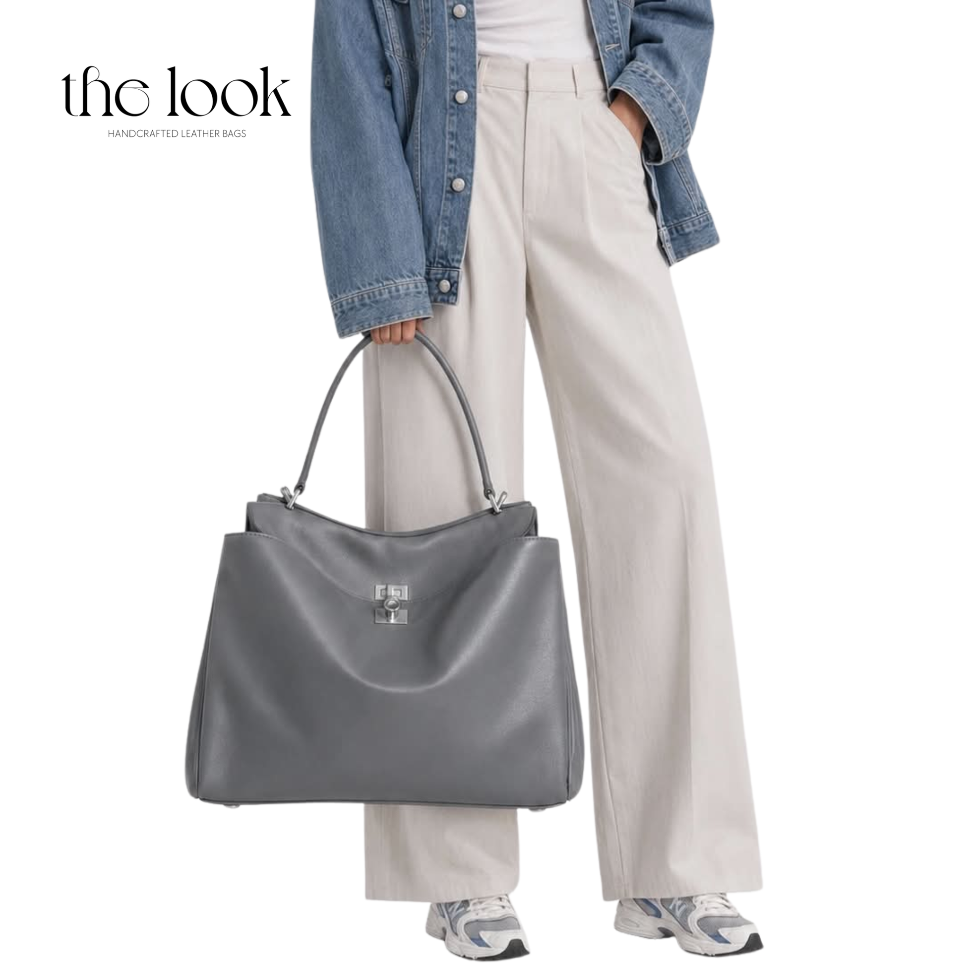 A gray leather tote bag with a silver-tone, held by a model wearing a denim jacket, cream wide-leg trousers, and sneakers.