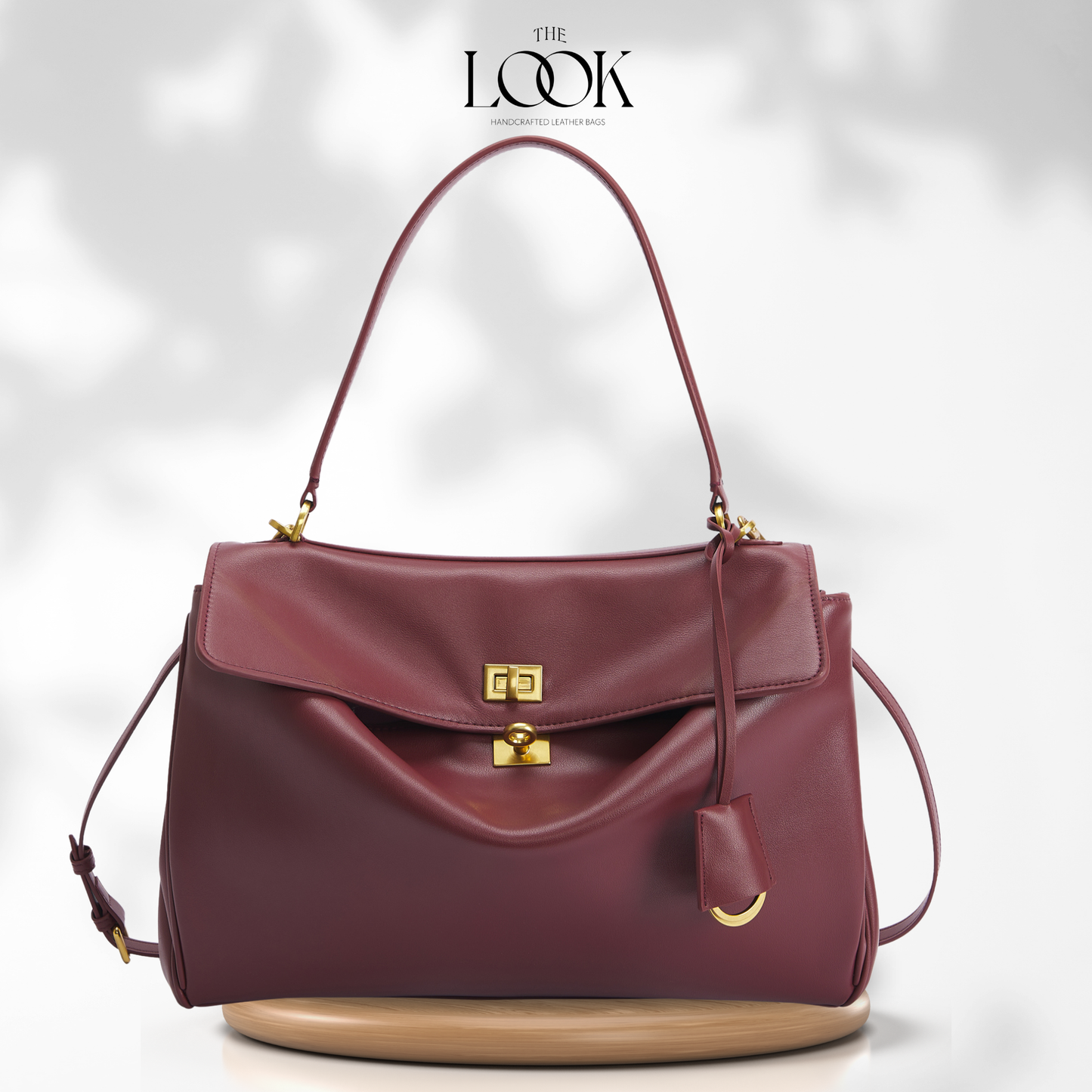 A burgundy leather handbag with gold-tone hardware, featuring a top handle, a flap closure, and a small hanging charm,
